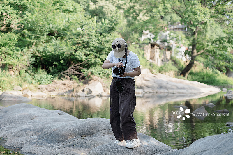 年轻女摄影师站在河中央的石头上用相机拍照图片素材