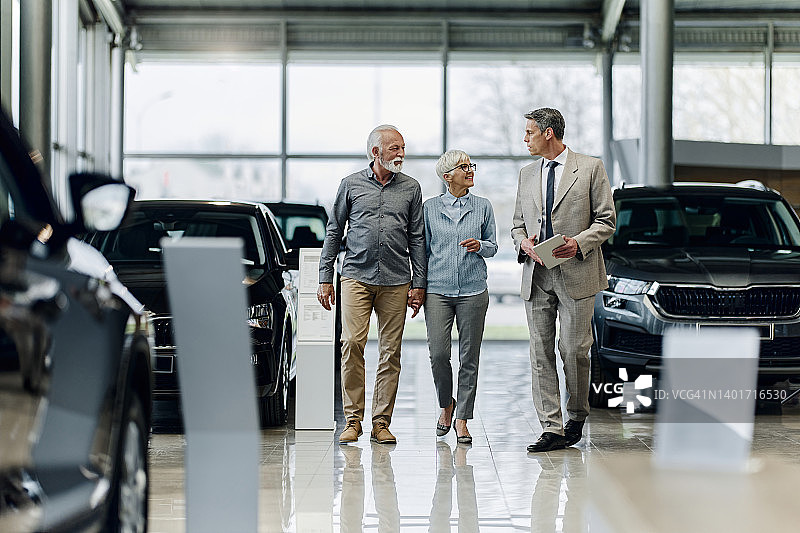 快乐的老年夫妇在展厅与汽车销售人员交谈。图片素材