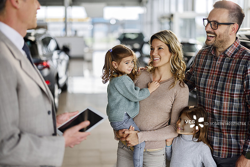 幸福的年轻家庭在展厅与汽车销售交谈图片素材