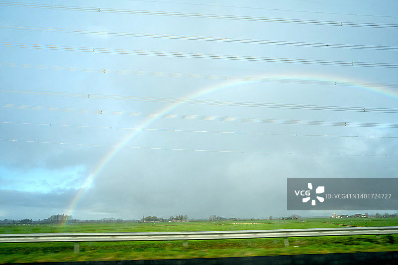 蓝色多云晴朗的戏剧性天空与彩虹，车窗或火车窗外视角，旅行概念，沿途电线图片素材