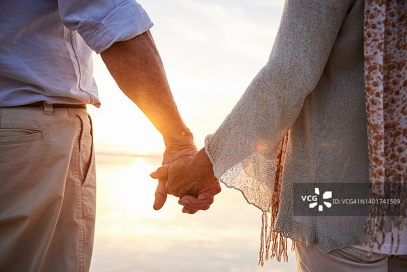 年长夫妇手牵手站在日落的海滩上图片素材
