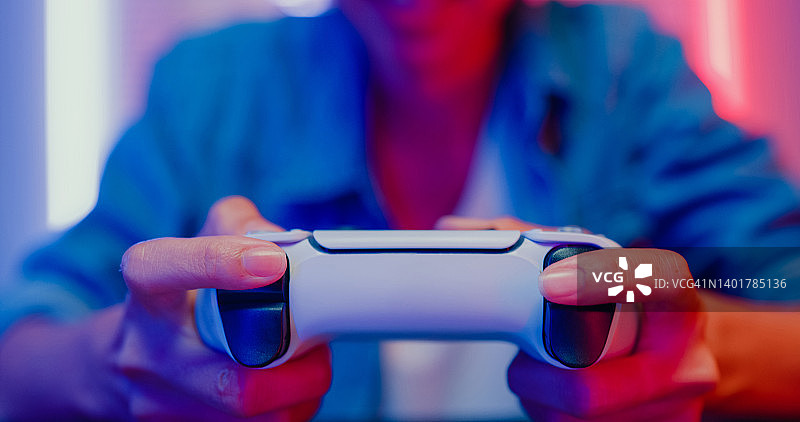 年轻亚洲女人在家中霓虹灯客厅玩电子游戏机的特写图片素材