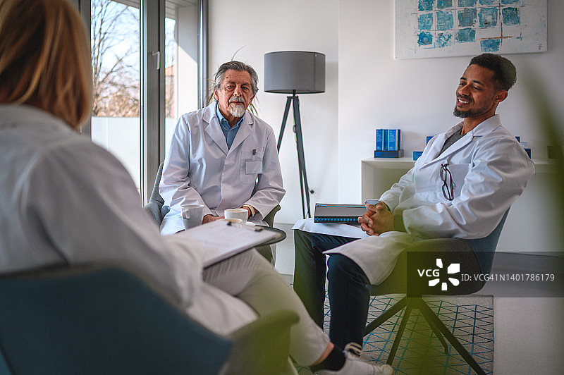 年轻的黑人男医生和年长的白人医生坐着讨论医疗报告图片素材