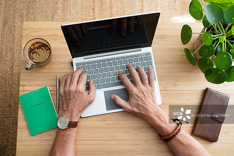 在家庭办公室里，一位不知名的男人正在笔记本电脑上打字图片素材