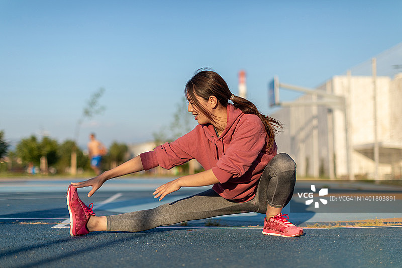 年轻休闲装女人在公共运动场伸展身体图片素材