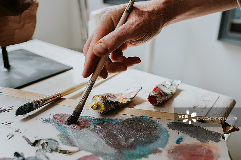手持画笔在调色板上混合油画颜料图片素材