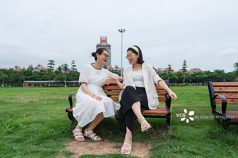 两位女士坐在公园长椅上愉快地聊天图片素材