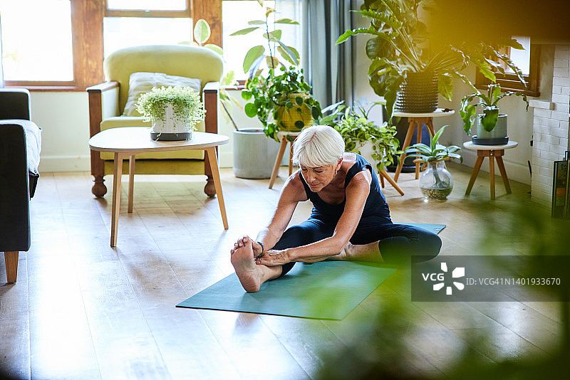 老年妇女在客厅地板上练习瑜伽时伸展身体图片素材