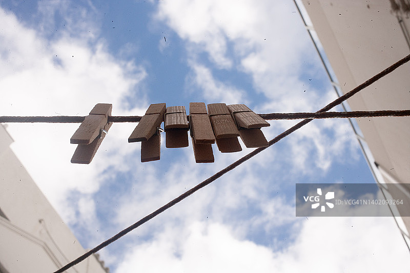 六个木制或竹制衣夹夹在空洗衣绳上的横向景观：从下方拍摄，显示出多云的蓝色天空，展现晾晒衣物的完美一天图片素材