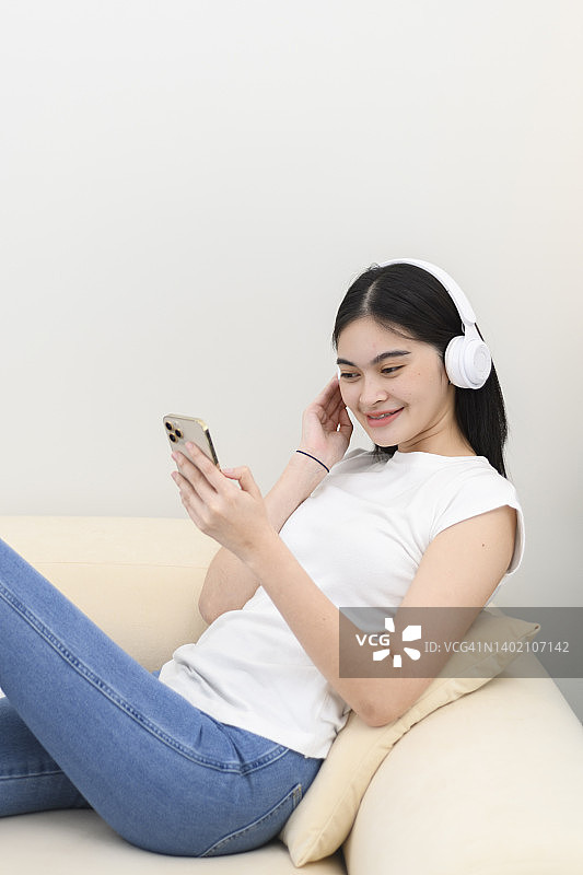 年轻女人戴着耳机，在沙发上用智能手机听音乐图片素材