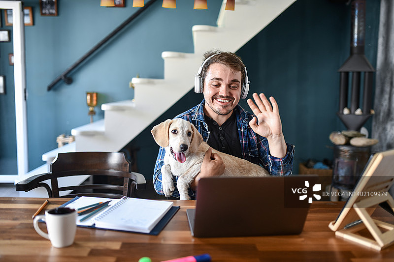 微笑的自由职业男士和他的狗在视频会议中向客户挥手图片素材