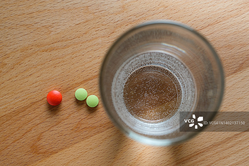 木桌上的红绿药丸和一杯水：维生素、止痛药和膳食补充剂，疾病预防、治疗和孕期准备概念图片素材