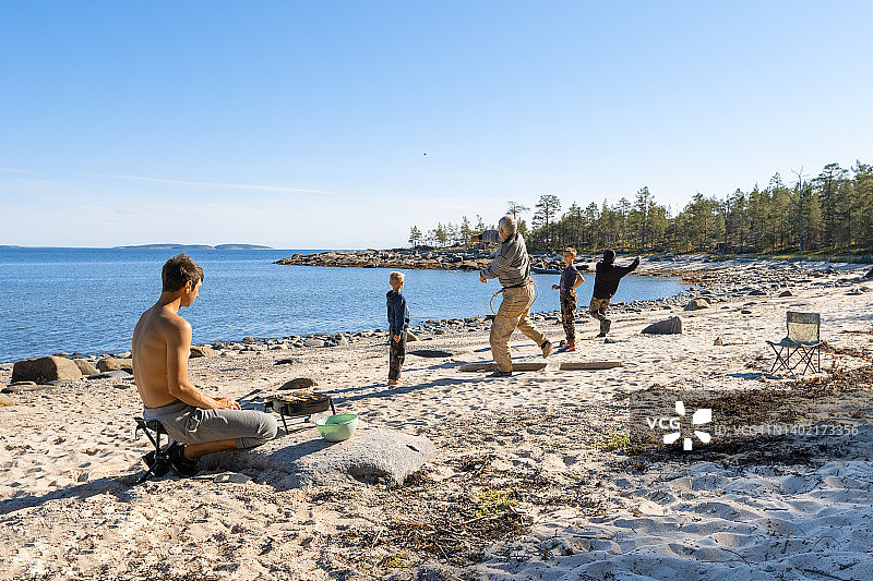全家在大型湖泊的沙滩上野餐，爷爷和孙子们在旅行中向水中扔石头玩耍图片素材