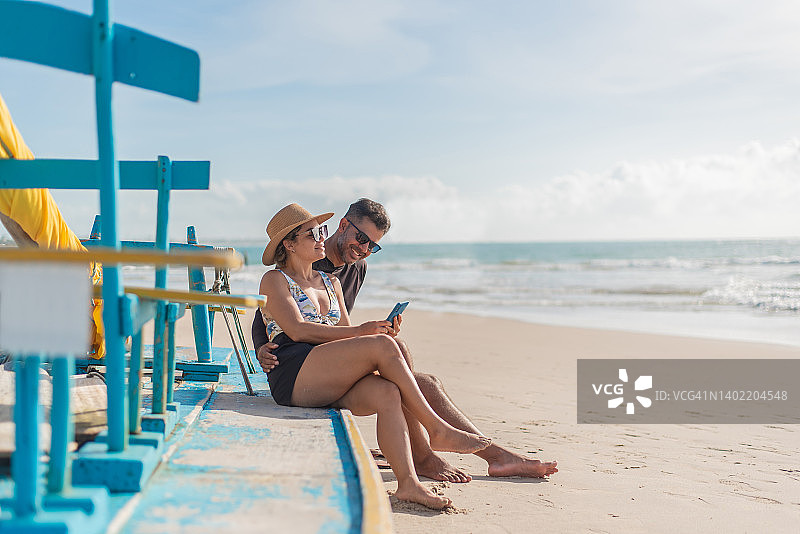 情侣在海滩上使用智能手机图片素材
