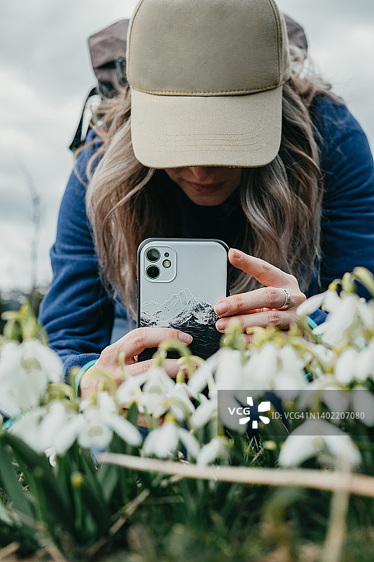 戴着帽子用手机拍摄鲜花的年轻女孩图片素材