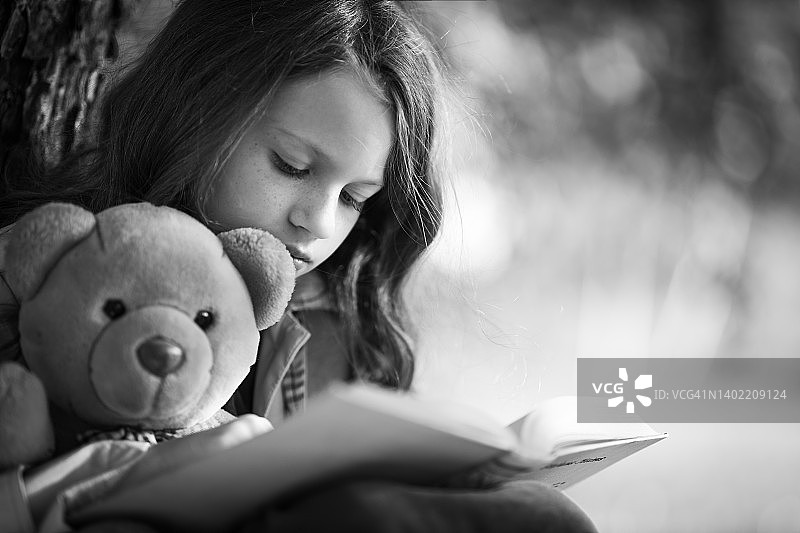 女孩和泰迪熊一起阅读故事书图片素材