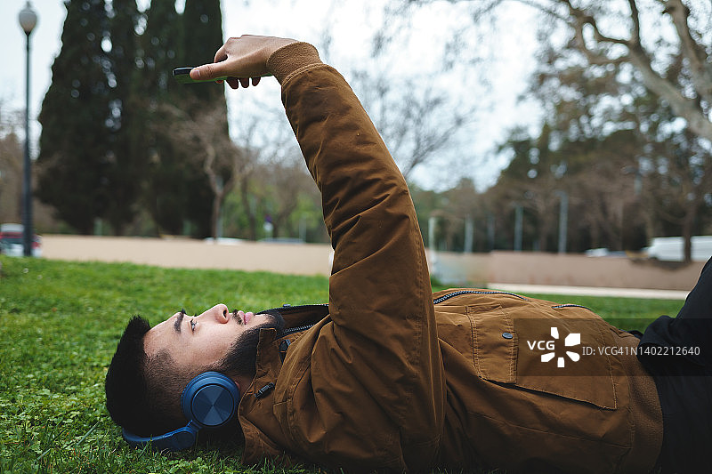 躺在公园里戴着耳机看手机的亚洲男人图片素材