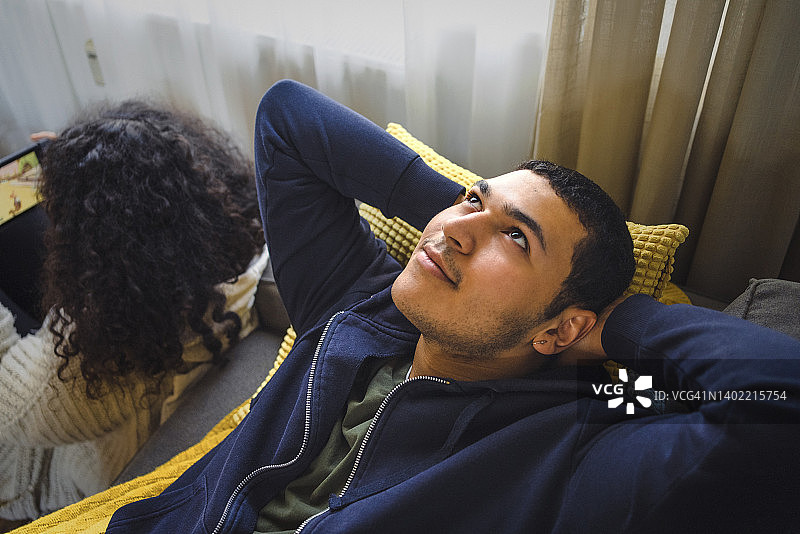 深思的男友躺在沙发上，双手放在女友身后的头上图片素材