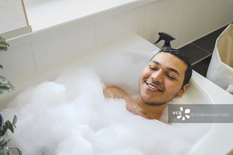 微笑男人在家中浴缸里泡澡的俯视图图片素材