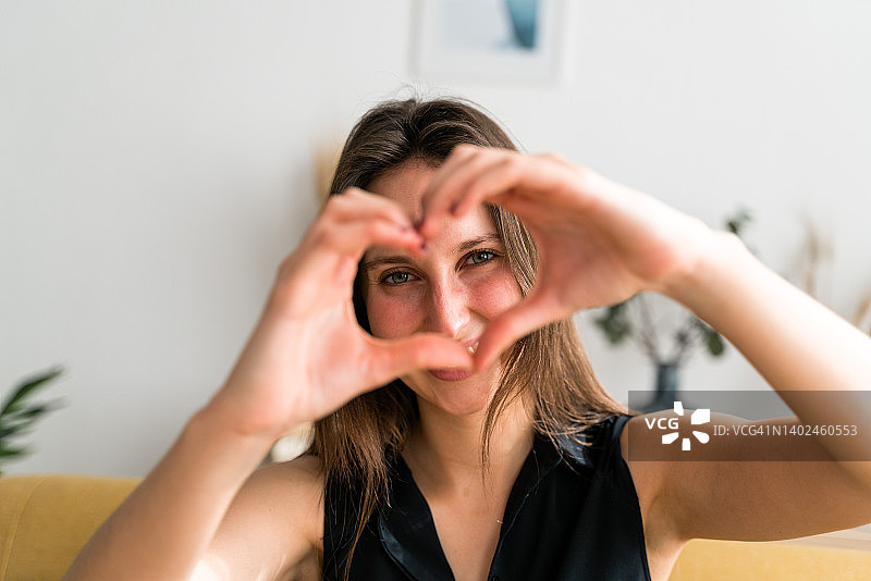 快乐的女人看着镜头，用手摆出心形，在室内摆姿势图片素材