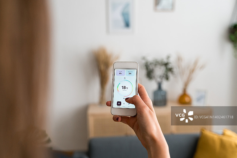 女人在家中使用手机上的应用程序设置室内温度图片素材
