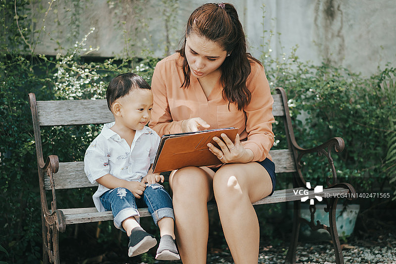 泰国女人和儿子坐在花园里使用平板电脑图片素材