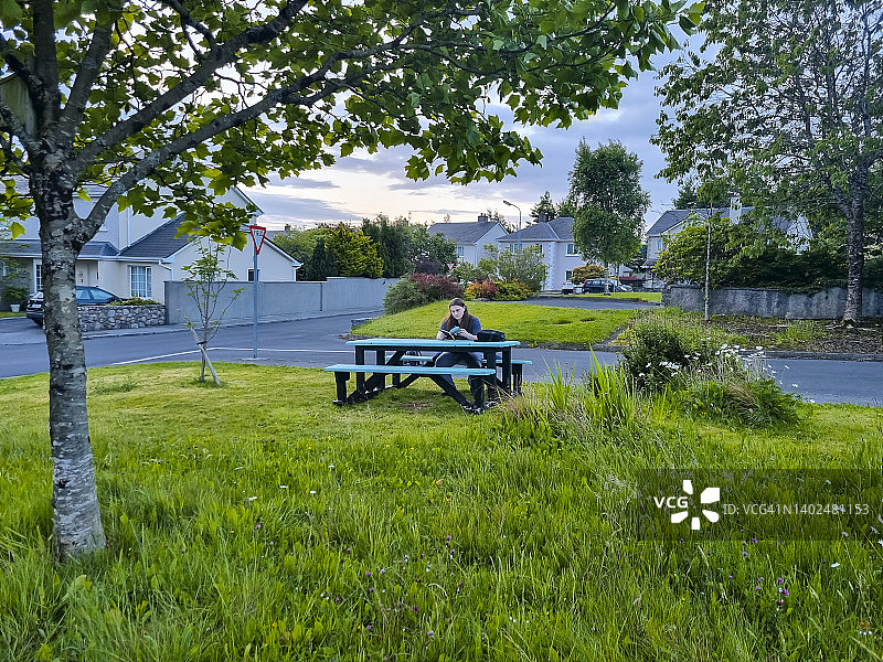 带公园长椅的开阔绿地，年轻男人坐着看书，户外放松图片素材