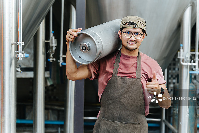 现代啤酒厂里，穿着皮围裙的男酿酒师拿着装满精酿啤酒的桶图片素材