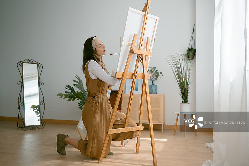 年轻艺术家在家中工作室跪着绘画的侧视图图片素材
