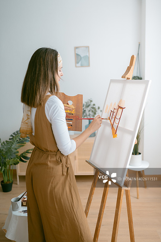 女艺术家在画室的木制画架前在画布上绘画图片素材