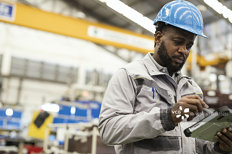 在制造业中使用物联网应用，降低成本、优化资源利用和减少浪费。一位非洲裔美国工厂主在生产线上使用数字平板电脑监控注塑机的状态图片素材