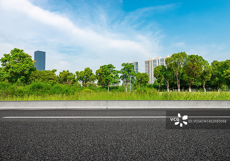 穿过茂密森林边缘的沥青公路，晴朗天空和浓密的白云图片素材