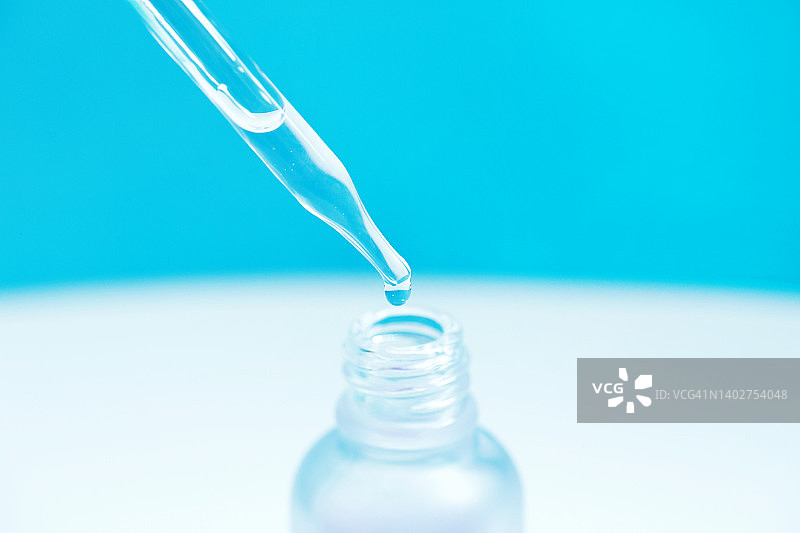 滴管将带气泡的精华滴入玻璃瓶，背景为白色和浅蓝色图片素材