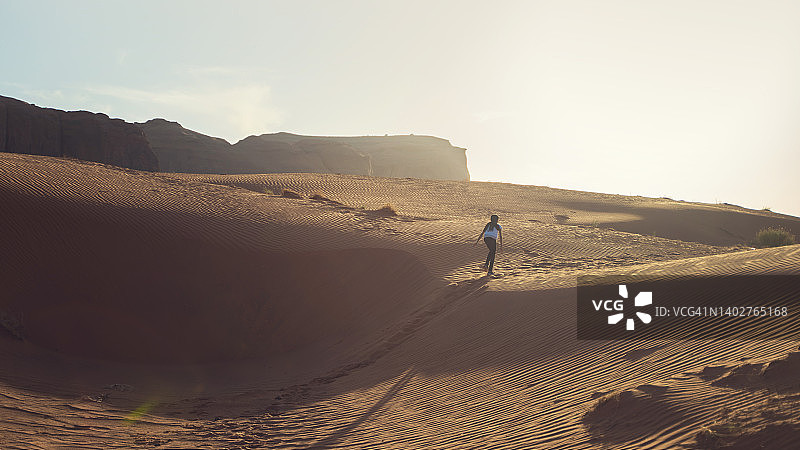 日落时分在美国犹他州纪念碑谷沙丘上奔跑的女孩图片素材