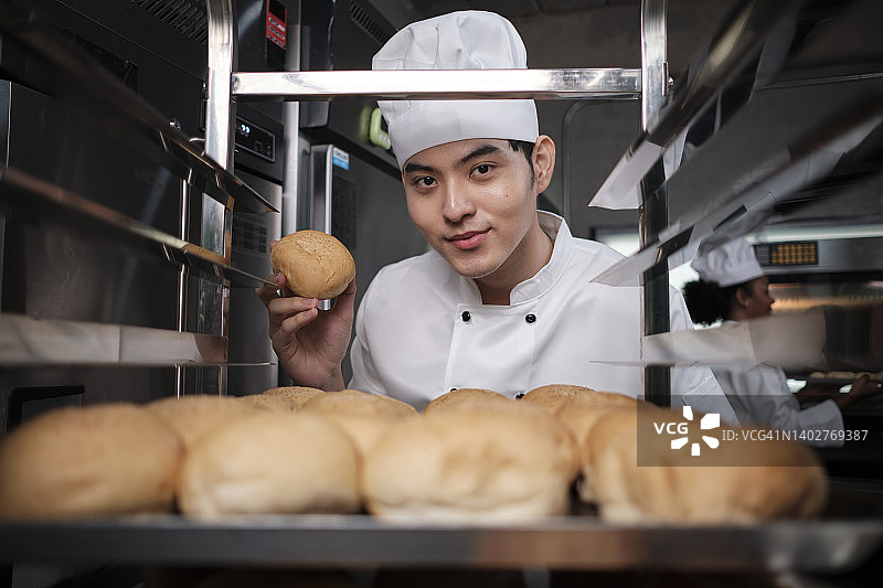 年轻的厨师在不锈钢厨房里笑着展示新鲜面包图片素材