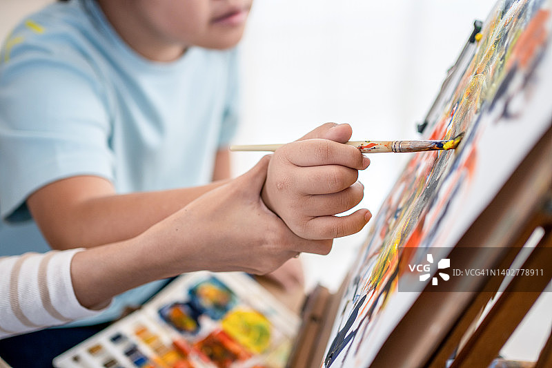 一位年轻的美术老师帮助自闭症儿童在画布上绘画。图片素材