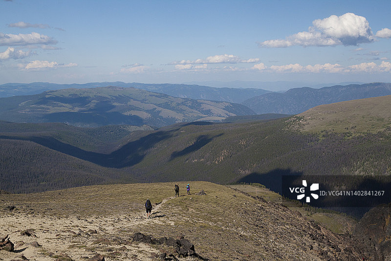 三个背包客在徒步旅行后返回山谷图片素材