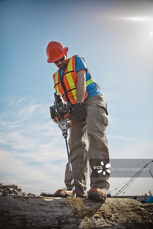 男人使用汽油动力螺旋钻在原木上钻孔图片素材