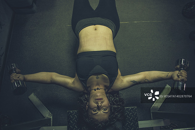 身体积极的女人躺在健身凳上，在健身房做举重哑铃锻炼图片素材