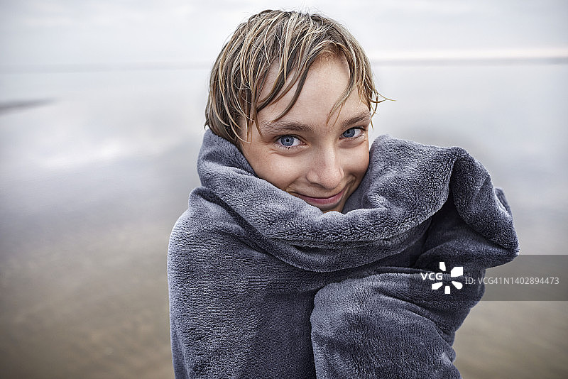 在海滩上手里拿着毯子的湿发男孩肖像图片素材