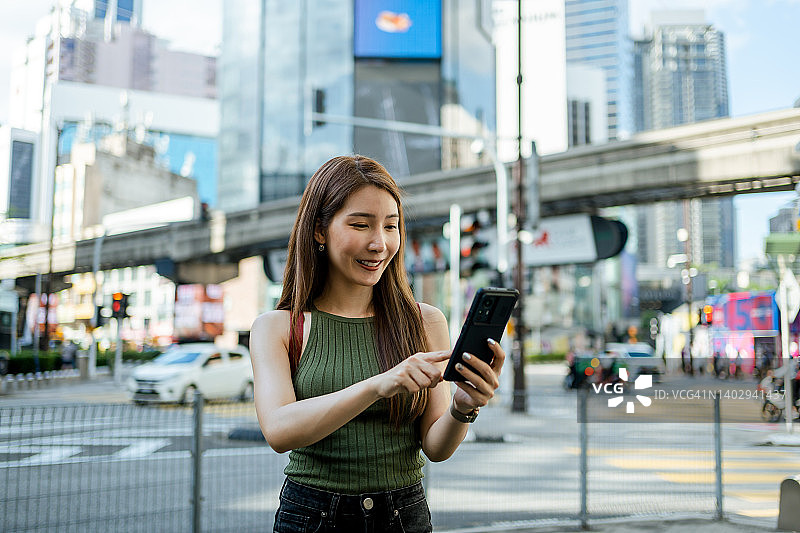 在马来西亚吉隆坡武吉免登十字路口使用智能手机的亚洲女性图片素材