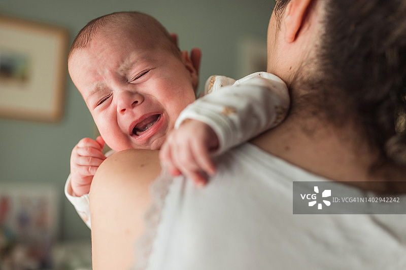 在母亲怀里哭泣的疲惫婴儿的特写图片素材