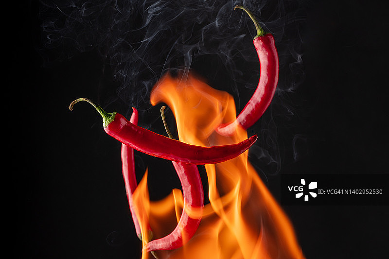 黑色背景上带有火焰的飞行的红辣椒图片素材