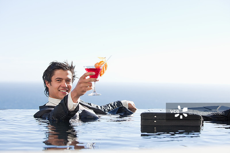 快乐的商人在游泳池里喝着鸡尾酒放松图片素材