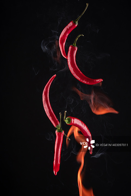黑色背景上带有火焰的飞行的红辣椒图片素材