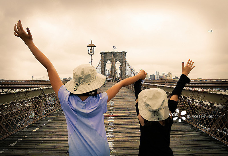 两个年轻女孩在布鲁克林大桥上向飞过的飞机挥手——纽约曼哈顿图片素材