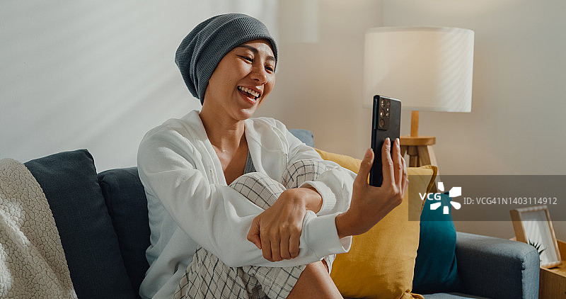 年轻亚洲女性癌症患者在家中客厅沙发上与朋友用电话交谈图片素材
