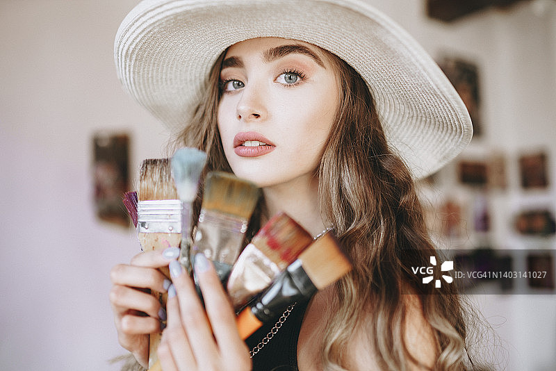 艺术家选择画笔——年轻女画家在工作室手持画笔图片素材