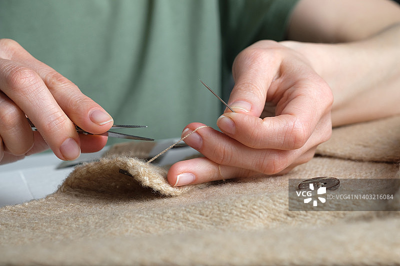 女人在针织毛衣、开衫或外套上缝一颗纽扣，用剪刀剪断线，缝纫师、家庭主妇或裁缝手中的针线，真实的生活方式，爱好，手工制作，女人的家务概念图片素材