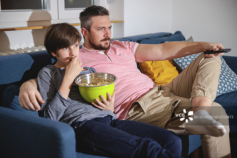 和儿子一起坐在沙发上看电视的严肃男人图片素材